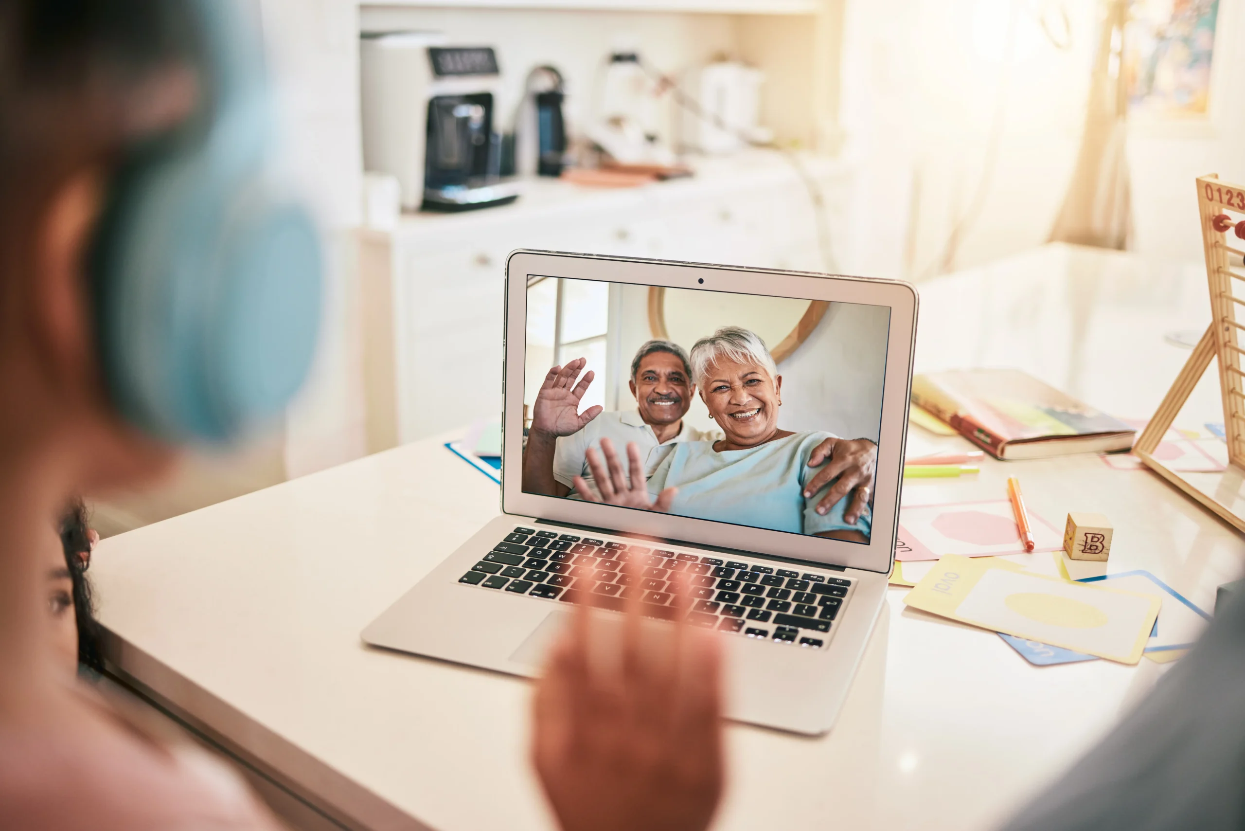 An elderly senior couple smiling and waving during a virtual speech-language pathology teletherapy video call on a laptop.