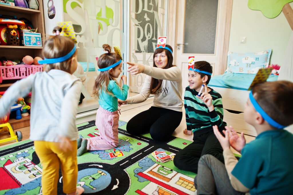 A speech-language pathologist or educator playing a headband guessing card game with a group of young children during a therapy session.