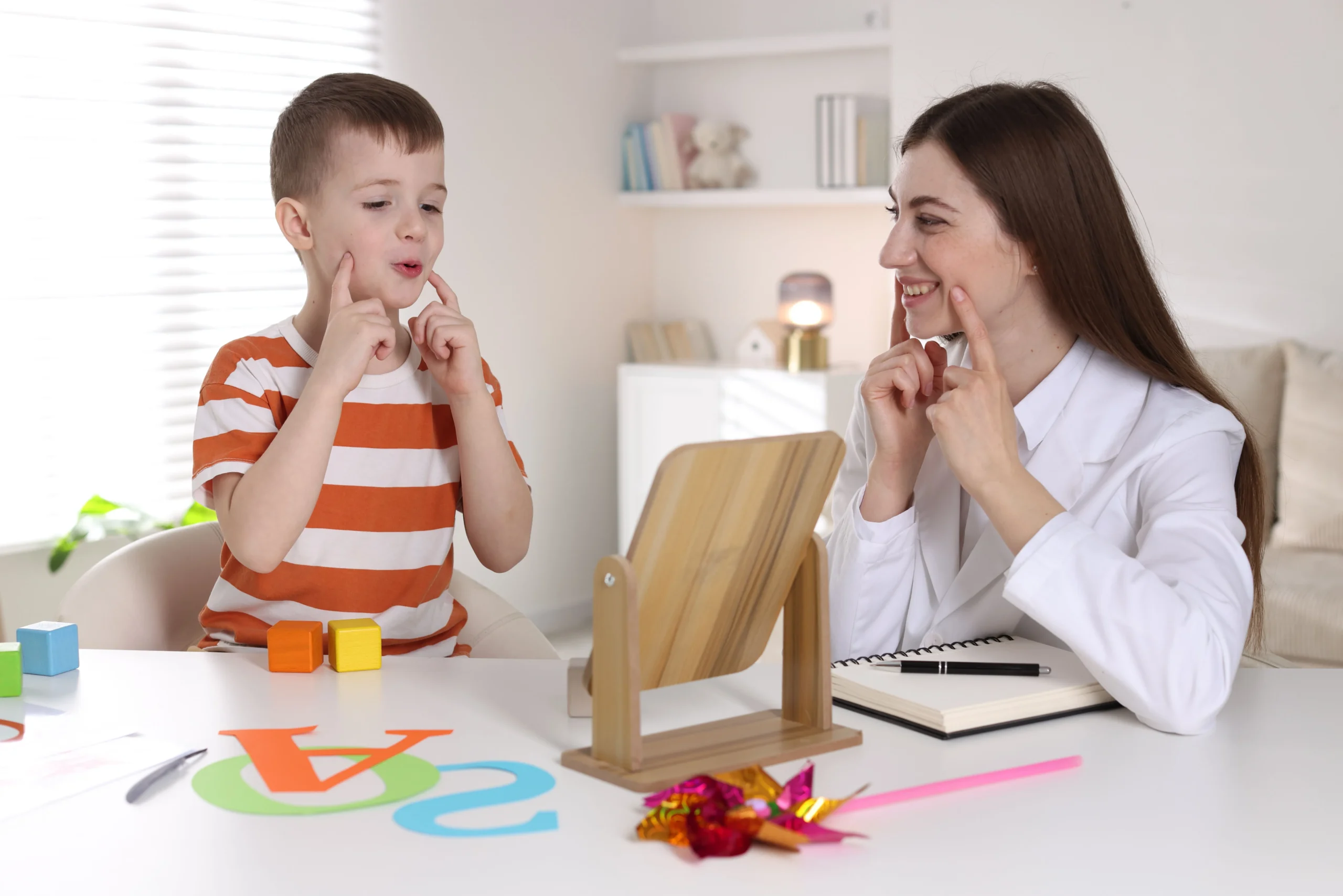 A young boy mirrors his female speech-language pathologist's mouth movements and facial expressions during a speech therapy articulation exercise.