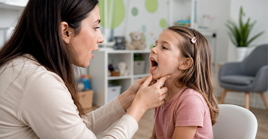 A speech therapist gently holding a young girl's chin while examining her tongue elevation during an assessment.